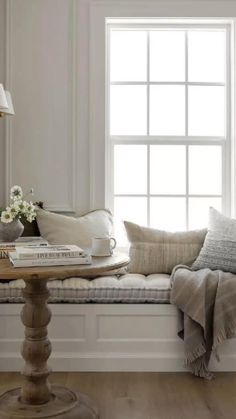 a window seat with pillows and blankets on it in front of a white painted wall