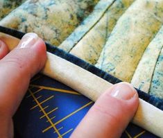 a person's hand on top of a blue and yellow piece of cloth next to a quilt