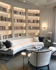 a living room filled with lots of white furniture and bookshelves full of books