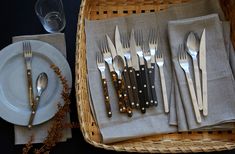 a basket with silverware on top of it next to plates and utensils