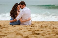 a man and woman are sitting on the sand at the beach looking into each other's eyes