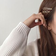 a woman with long brown hair wearing a white sweater and holding her hair in one hand