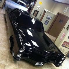 a black car is parked in the middle of a room with other cars on display