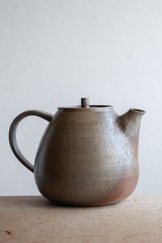 a brown teapot sitting on top of a wooden table next to a white wall