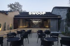 an outdoor restaurant with black tables and chairs in front of the entrance to the building