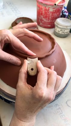 two hands are working on a clay bowl with a piece of wood sticking out of it