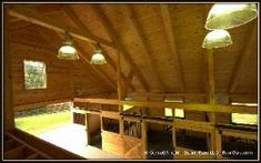 the inside of a horse barn with several stalls and lights hanging from it's ceiling