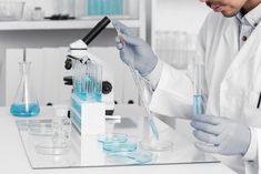 a male in a white lab coat is holding some blue liquid and looking at it