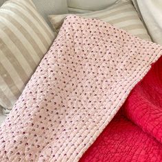 a pink blanket is laying on top of a bed next to two pillows and a striped pillow case