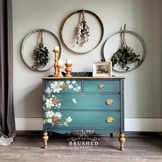 a blue dresser with flowers painted on it and two round mirrors hanging above the drawers