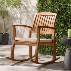 a wooden rocking chair next to a potted plant on a patio with a candle