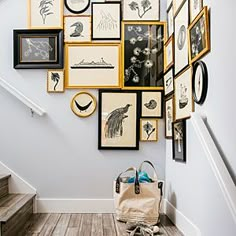 a bunch of framed pictures are hanging on the wall above a stair case with a handbag next to it