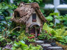 a small house made out of straw with plants and flowers around it in the garden