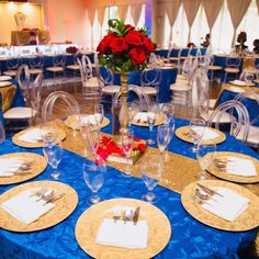 a blue table cloth with gold place settings and red roses in vase on the center