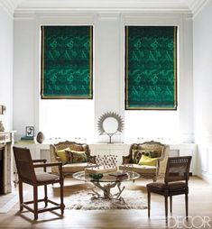 a living room filled with furniture and two large windows covered in green drapes