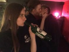 two men and a woman drinking wine in a dimly lit room with red lights behind them