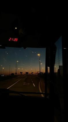 the view from inside a bus at night with street lights and traffic signs in the distance