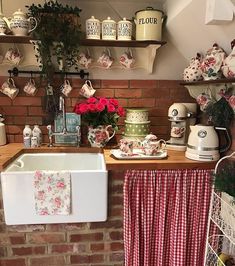 a kitchen with red and white checkered curtains on the window sill next to a brick wall