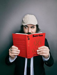 a man reading a book while wearing a hat and holding it up to his face