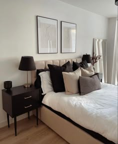 a bed with white sheets and pillows in a bedroom next to two framed pictures on the wall