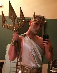 a man dressed up as an ancient greek god holding a cell phone in his right hand