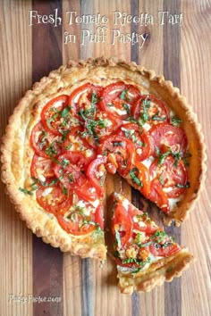 a fresh tomato tart on a wooden cutting board with a slice missing from it