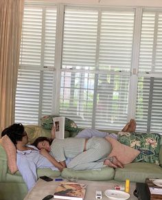 two people laying on couches in front of windows with blinds open and one person sleeping