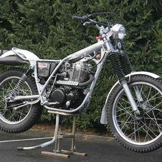 a motorcycle is parked in a parking lot next to some bushes and shrubbery on the side of the road