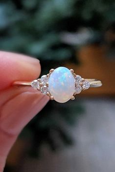 a woman's hand holding an opal and diamond ring