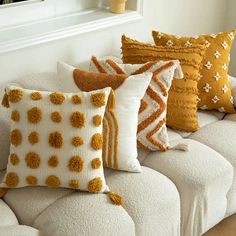 a couch with several pillows on it in front of a mirror and vase filled with flowers