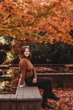 a woman sitting on top of a bench in front of trees with leaves around her