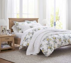 a bed with white linens and yellow flowers on it, in a bedroom setting