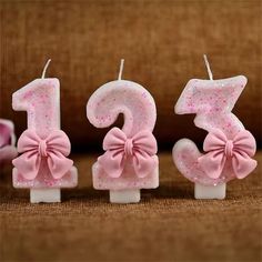 three candles with pink bows on them sitting next to each other in the shape of numbers