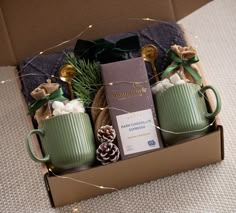 two green mugs filled with coffee and marshmallows in a gift box