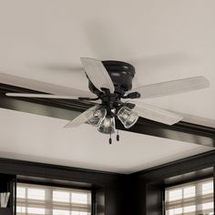 a black ceiling fan with three white blades and four light bulbs on it in a living room