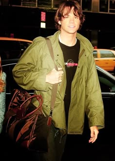 a young man carrying a brown bag and wearing a green jacket