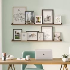 a laptop computer sitting on top of a wooden desk next to a green chair and framed pictures