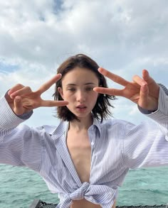 a woman standing in front of the ocean holding her hands up