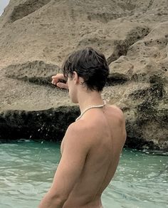 a shirtless man standing in the water with his hand on his head and looking off into the distance