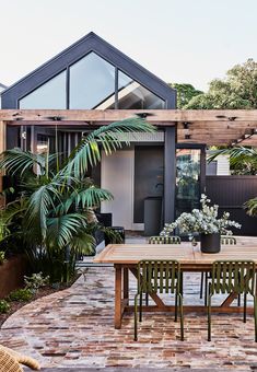 an outdoor dining table and chairs in front of a house with large plants on the patio