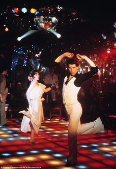 two people dancing on a dance floor with disco lights in the background and one person wearing a white dress