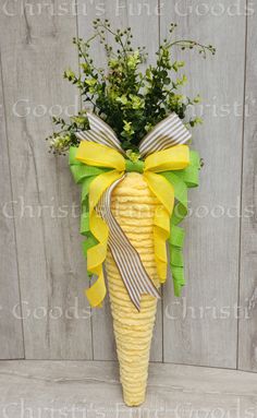 a corn cob with yellow and green ribbons tied around it, hanging on a wooden fence