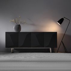 an empty room with a black cabinet and lamp on the sideboard next to it