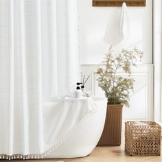 a white bath tub sitting next to a wooden basket filled with plants and soap bottles