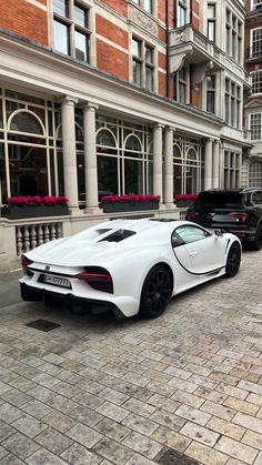 a white sports car parked in front of a building on a brick street next to tall buildings