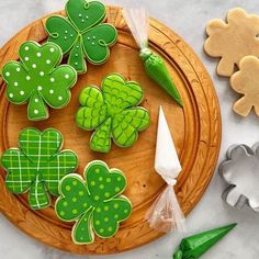 cookies decorated with green shamrocks on a wooden platter next to cookie cutters