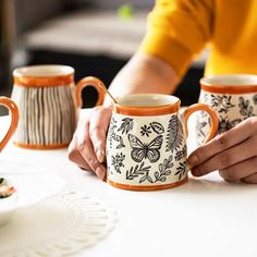 two people are holding coffee mugs on a table