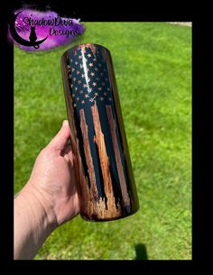 a person holding up a black and brown american flag tumbler cup in their hand