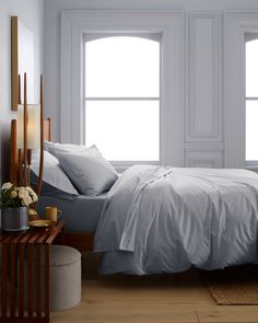 a bed with white sheets and pillows in a bedroom next to two large windows on the wall