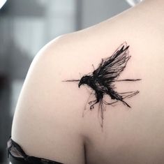 the back of a woman's shoulder with a black bird tattoo on her left shoulder